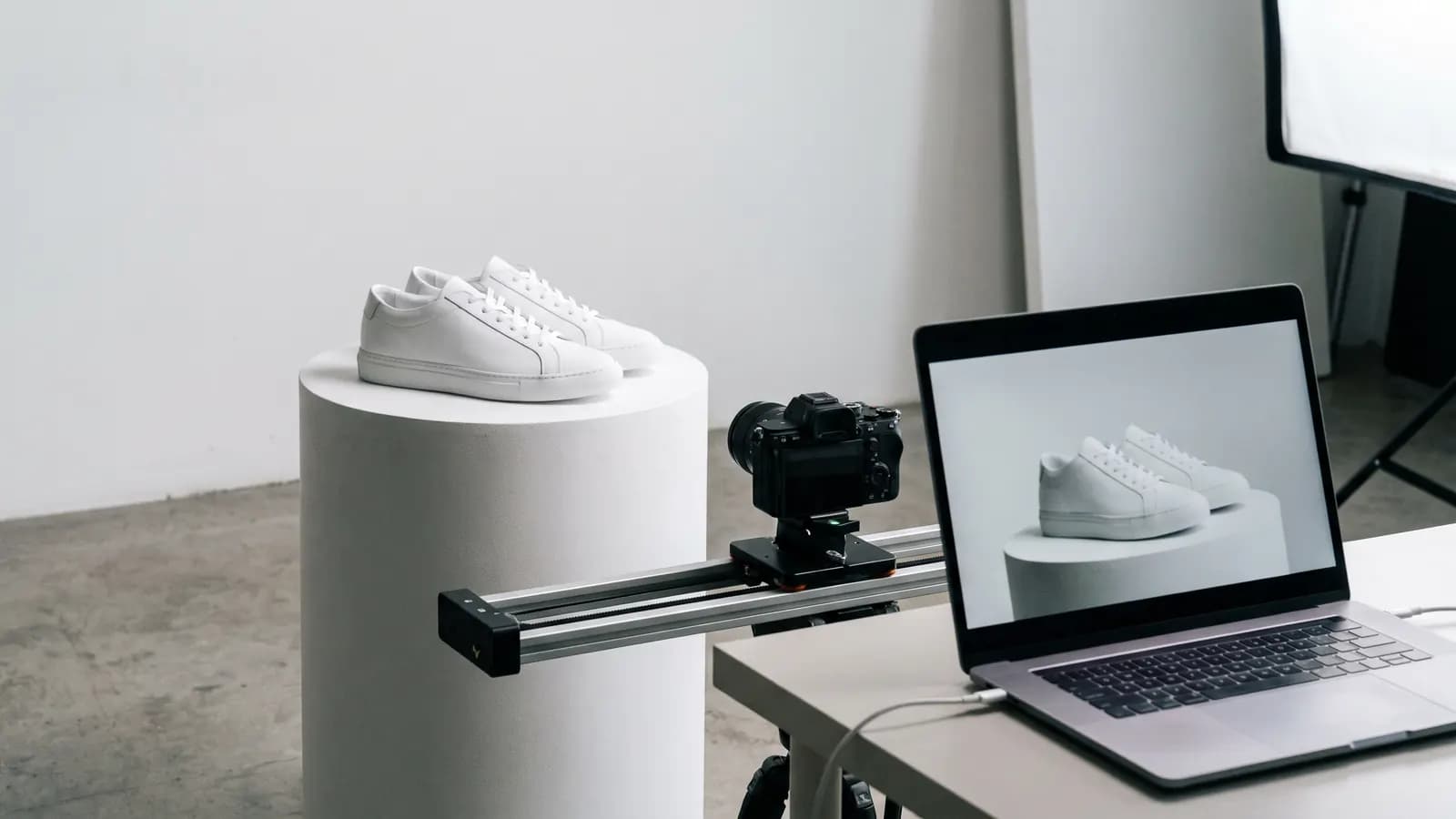 White sneakers on a pedestal, a camera on a slider beside them and a laptop showing a clip of the same sneakers